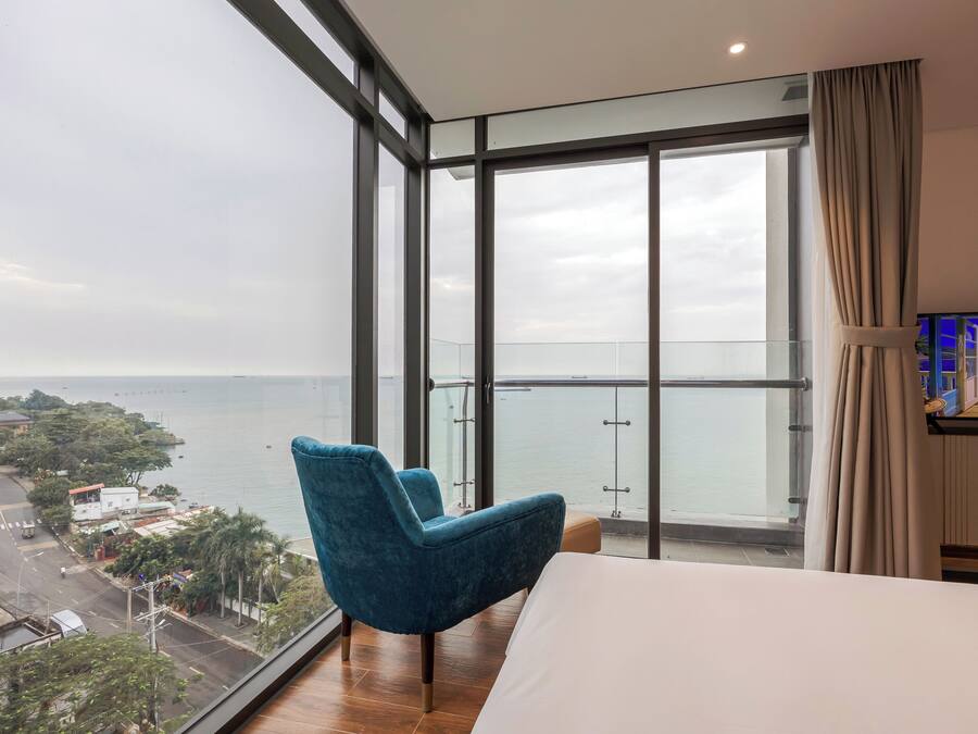Una habitación de hotel con un ventanal grande, una cama, una silla azul y un televisor.
