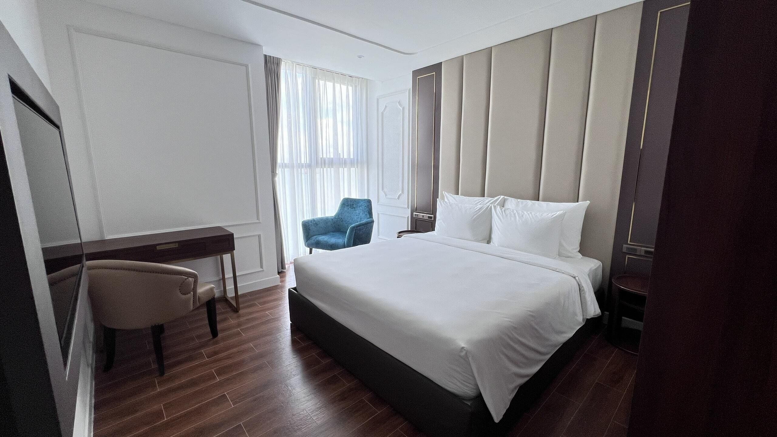 A hotel room with a large bed, a desk, a chair, and a window with curtains.