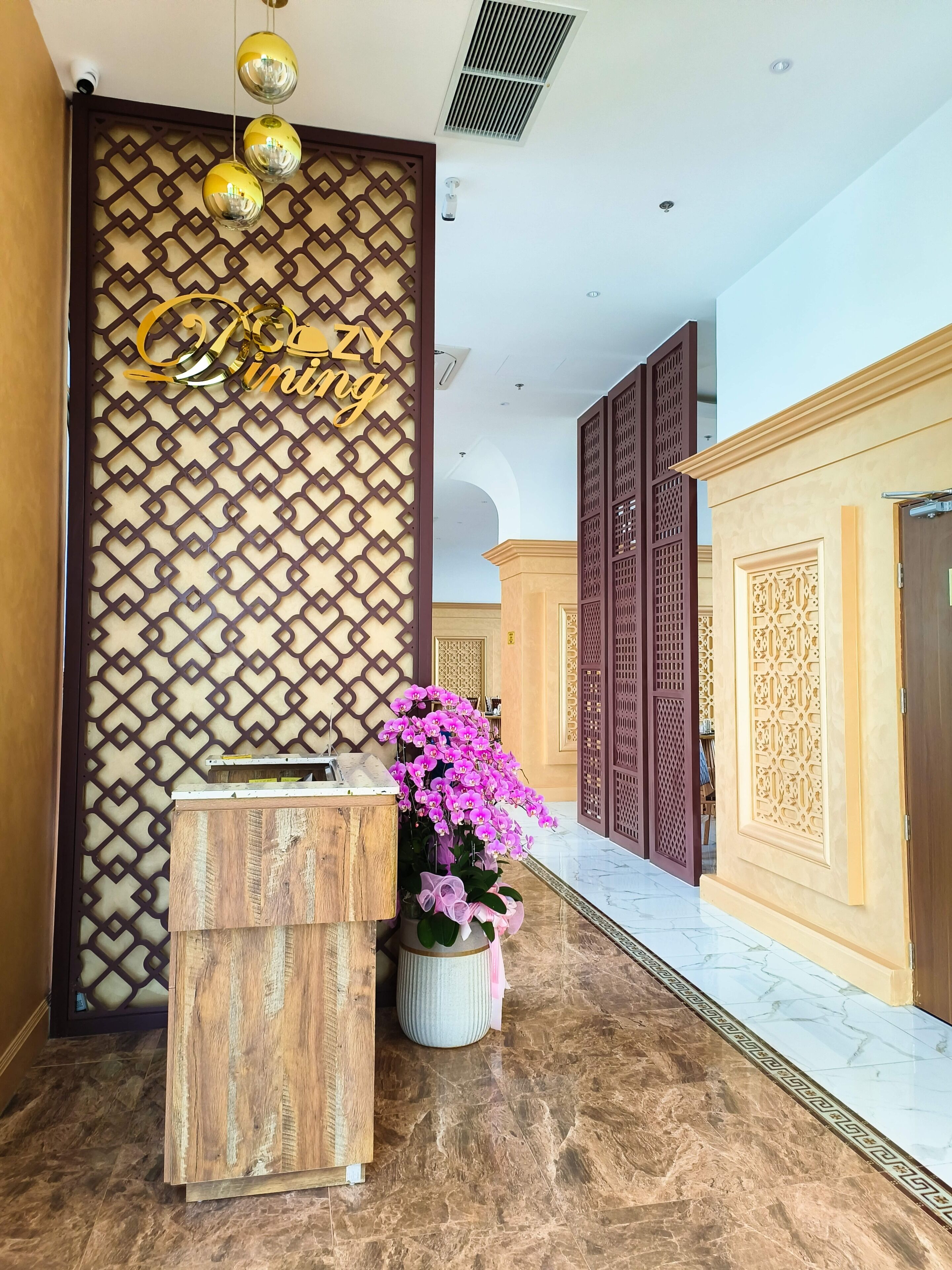 A reception area with a wooden desk, a potted orchid, and a decorative wall with a geometric pattern.