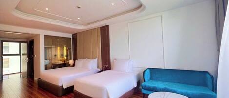 Habitación de hotel con dos camas, un sofá azul, una mesita redonda y un espejo grande.