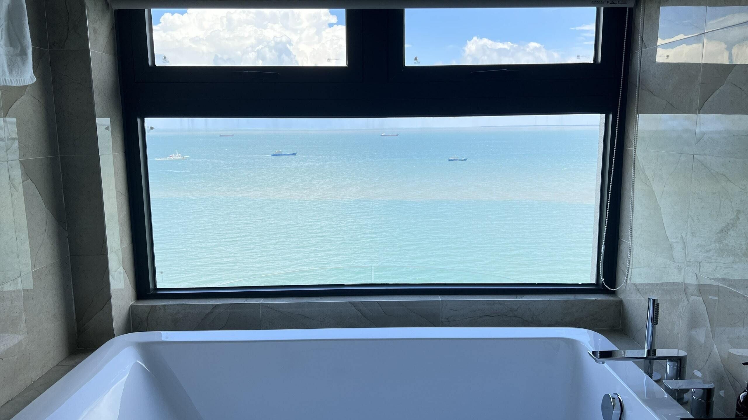 Un baño con una bañera grande y vista al océano a través de una ventana.