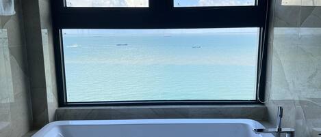 Un bagno con una vasca da bagno ampia e vista sull'oceano attraverso una finestra.