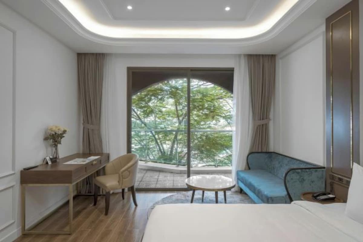 Une chambre d’hôtel moderne dotée d’un grand lit, d’un bureau, d’un canapé et d’un balcon offrant une vue sur les arbres.