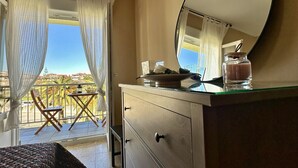 Une chambre d’hôtel avec un balcon, un miroir rond, une commode et une petite table avec une bougie.