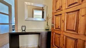 Une pièce avec une porte en bois, un bureau avec un miroir et un vase posé sur le bureau.