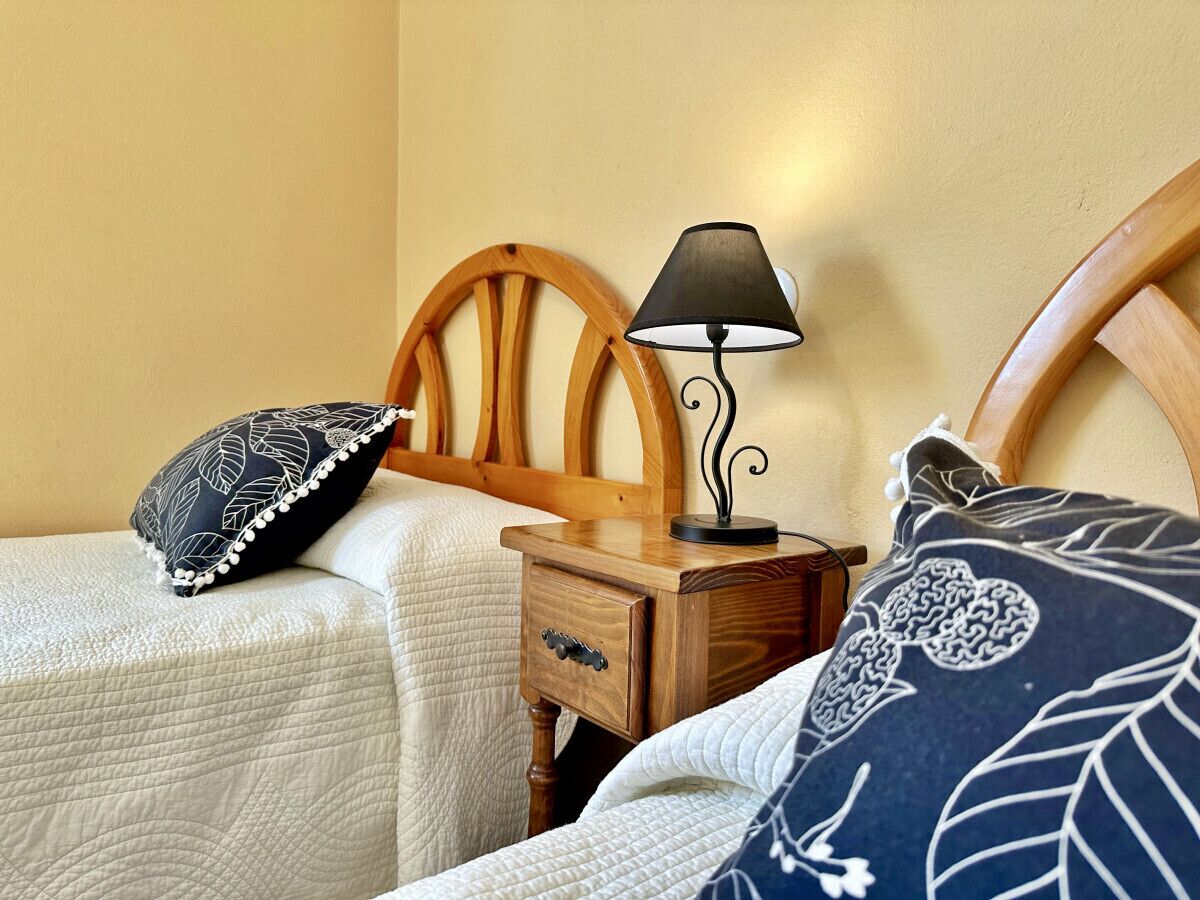 A bedroom with two single beds, a wooden headboard, a nightstand with a lamp, and a bedside table with a drawer.