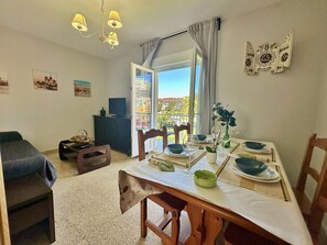 A dining area with a table set for two, a sofa, and a view of the outdoors. - Bajo con Jardín y Barbacoa - La Esteluca 6805 (Noja)