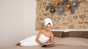 A person lying on a bed with a book, in a room with a stone wall and decorative wall art. - B&B Sotto le Mura Wellness (Pietramontecorvino)