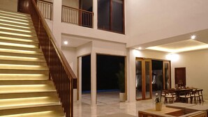 A spacious living area with a wooden staircase, a dining area, and a large window. - Kanaka Villa Buahan (Payangan)
