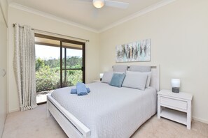 A bedroom with a bed, a nightstand, a ceiling fan, a window with curtains, and a painting on the wall.