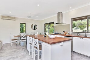 A modern kitchen with white cabinetry, a wooden island, and a large window offering a view of greenery. - Kookaburra Range (North Rothbury)