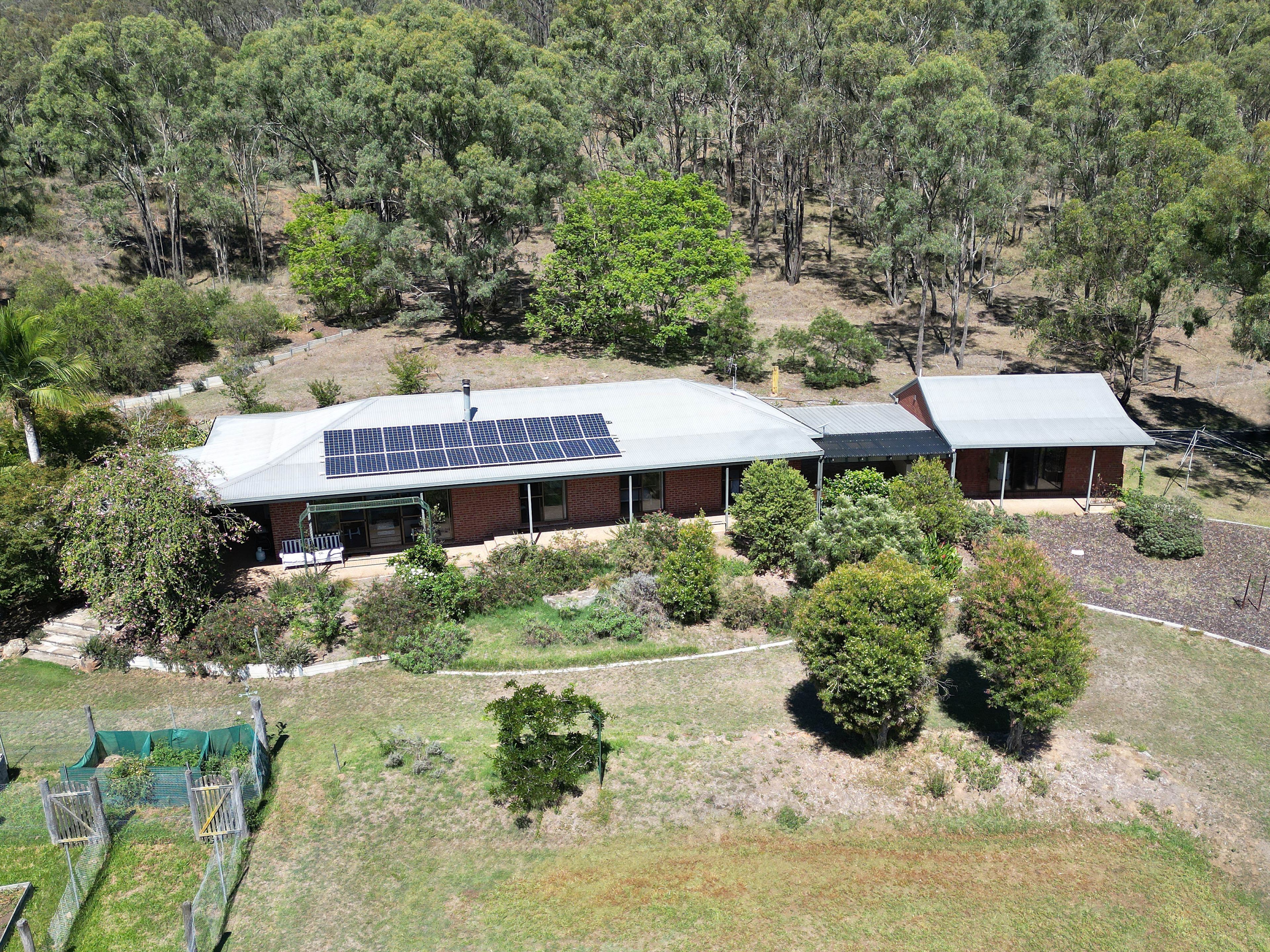 A two-story house with a solar panel roof, surrounded by trees and a grassy area.
