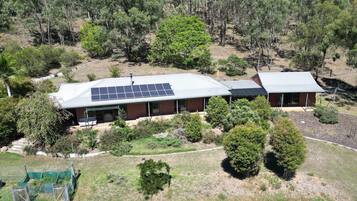 A two-story house with a solar panel roof, surrounded by trees and a grassy area.
