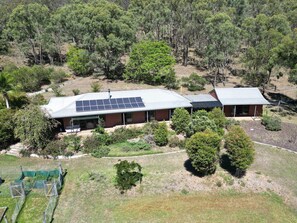 A two-story house with a solar panel roof, surrounded by trees and a grassy area.