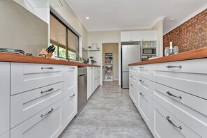 A modern kitchen with white cabinetry, a wooden countertop, and a brick accent wall. - Kookaburra Range (North Rothbury)