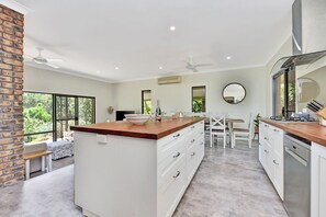 A modern kitchen with a central island, white cabinetry, and a brick accent wall. - Kookaburra Range (North Rothbury)