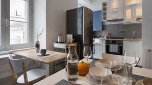 A modern kitchen with white cabinets, a black refrigerator, and a dining area with a table set for two. - La Casa in Viale, short term rent apartment (Trieste)