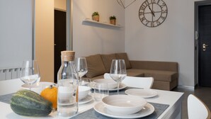 A dining table set with plates, glasses, and a bottle, with a clock and plants on the wall. - La Casa in Viale, short term rent apartment (Trieste)
