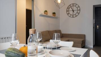 A dining table set with plates, glasses, and a bottle, with a clock and plants on the wall.