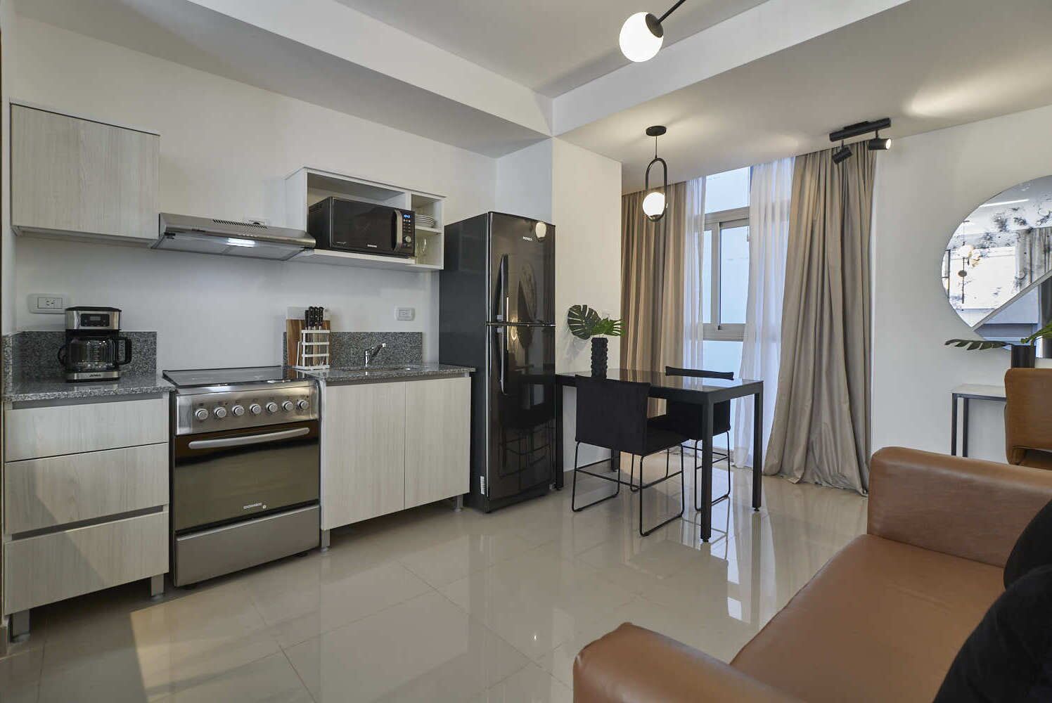 Una cocina moderna con electrodomésticos de acero inoxidable, una zona de comedor con mesa y sillas, y un ventanal con cortinas.