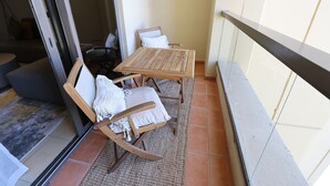 Un balcon avec une table en bois et deux fauteuils à bascule, un petit tapis et une vue sur l’extérieur.