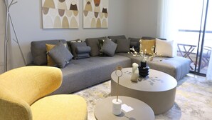 Un salon moderne comprenant un canapé, deux fauteuils, une table basse et des œuvres d’art abstraites accrochées au mur.