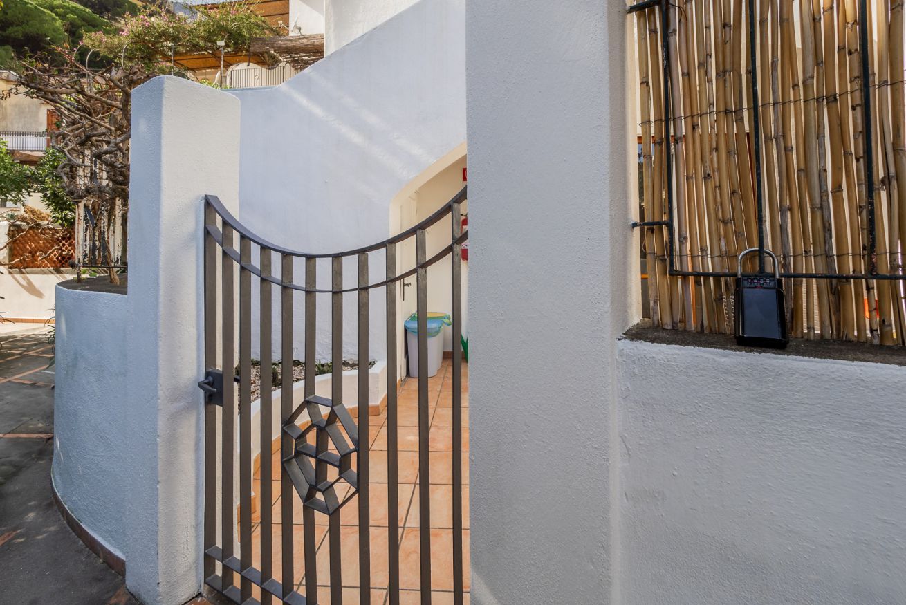 Una entrada protegida con un portón metálico, un muro blanco y una valla de bambú.