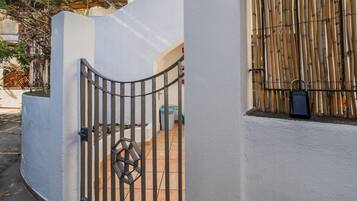 Una entrada protegida con un portón metálico, un muro blanco y una valla de bambú.
