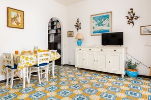 Un comedor con una mesa preparada para cuatro personas, un armario blanco con televisor y un suelo estampado.