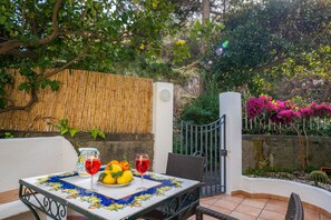 Une terrasse extérieure avec une table dressée pour deux personnes, une chaise en osier, une clôture en bambou et un portail.