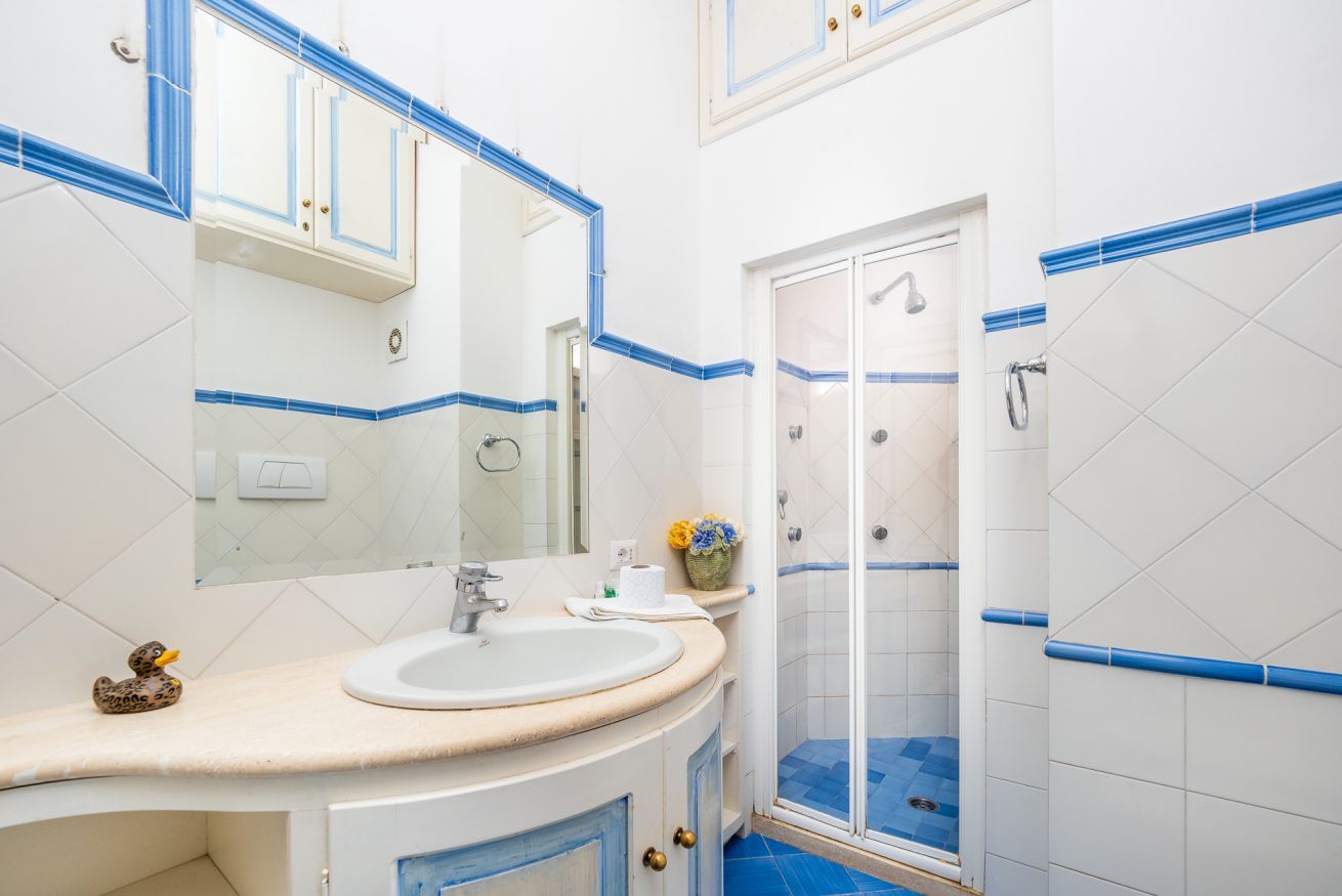 Un baño con lavamanos, espejo, ducha y paredes de azulejos azules.