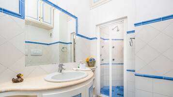 Un baño con lavamanos, espejo, ducha y paredes de azulejos azules.