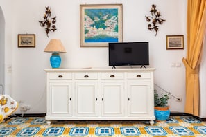 A white cabinet with a flat-screen TV on top, a blue vase, and a framed painting on the wall. - Casa Simona - Positano Center - 5 min to the beach (Positano)