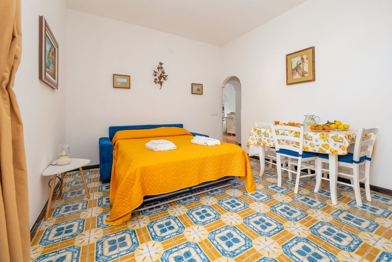 A room with a bed, a table with chairs, and a tiled floor.