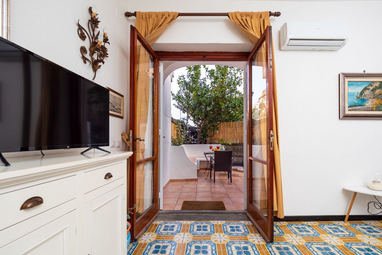 A room with a television on a white cabinet, a door leading to an outdoor area with a table and chairs, and a patterned floor.