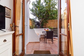 Une porte-fenêtre donnant sur un patio extérieur, avec une table et des chaises, un fauteuil en osier et un paillasson.