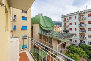 Un immeuble à plusieurs étages doté de balcons, d’un auvent vert et offrant une vue sur une colline.