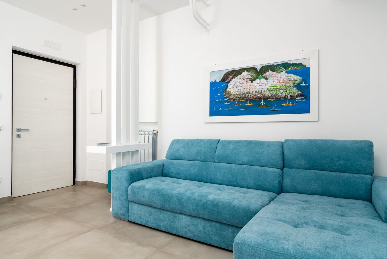 A room with a blue sofa, a white door, and a framed painting of a coastal scene.