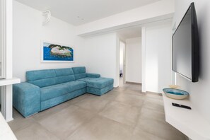 A modern living room with a blue sectional sofa, a flat-screen TV mounted on the wall, and a framed picture above the sofa.