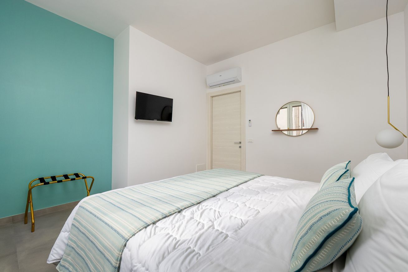 A bedroom with a bed, a television, a mirror, and an air conditioning unit.