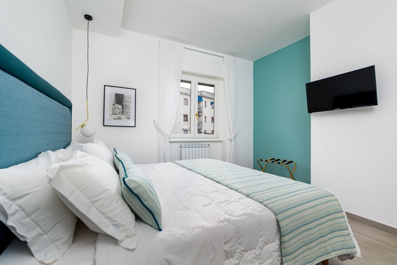 Un dormitorio con cama, ventana con cortinas, televisor montado y radiador.