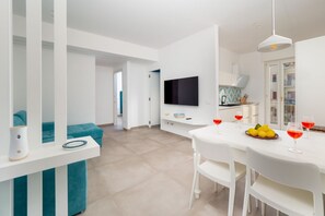 Een moderne keuken met een eethoek, een flatscreen televisie en een witte tafel gedekt met glazen en fruit.