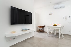 Una cuina moderna amb televisió de pantalla plana, taulell blanc i zona de menjador amb taula preparada per a dues persones.