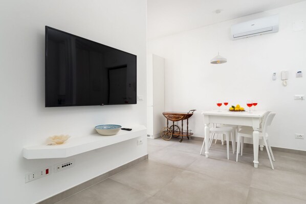 A modern kitchen with a flat-screen TV, a white countertop, and a dining area with a table set for two.