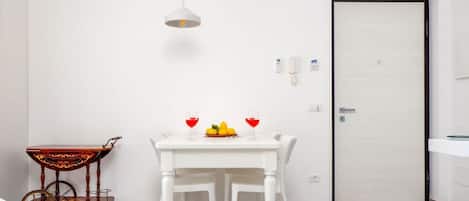 A white dining table with chairs, a fruit bowl, two wine glasses, and a vintage cart.