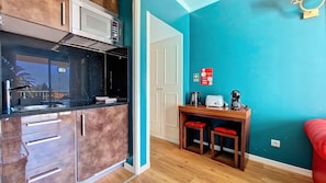 A compact kitchen with a microwave, stove, and sink. There's a wooden table with chairs and a red couch in the adjacent living area. - Ponta Beachside by LovelyStay (Funchal)