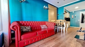 A red leather sofa with floral cushions, a wooden dining table, and chairs in a room with blue walls and wooden flooring. - Caracas Escape by LovelyStay (Funchal)