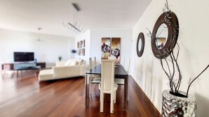 A modern living room with a dining area, featuring a wooden floor, white furniture, and decorative mirrors. - Sunset Bay by LovelyStay (Funchal)