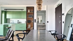 Een moderne keuken met groene kastjes, een eethoek met een lange tafel en stoelen, en een donkere deur met een handgreep.