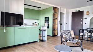 Een moderne keuken met groene kastjes, een eethoek met een tafel en stoelen, en een televisie op het aanrecht.